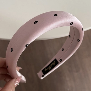 Macro detail of pink satin headband with black flower pattern and thick padded design