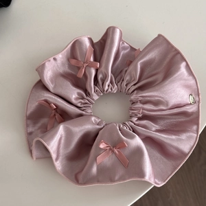 Detailed view of pink satin scrunchie with silk bows and a silver brand tag