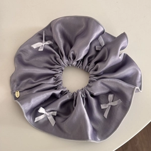 Close-up of lavender satin scrunchie with white bows and lucky metal tag detail