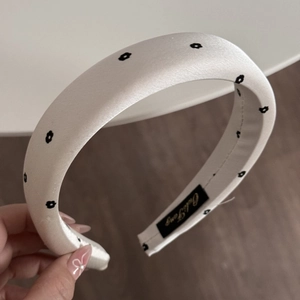 Close-up of white satin sponge headband with small black flower prints and label detail