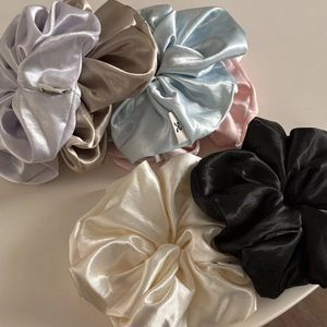 Detail of satin scrunchies set in pastel colors showing soft fabric texture and logo labels
