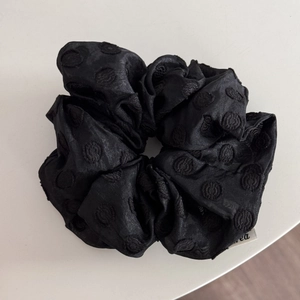 Detailed view of black satin scrunchie with circular textured weave and brand label tag