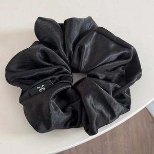 Close-up of oversized black satin scrunchie featuring a premium silky texture and brand tag