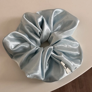 Detail of light blue oversized satin scrunchie with silk texture and woven label