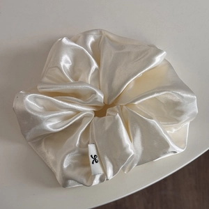 Detailed macro view of cream satin oversized hair scrunchie with silk texture and label