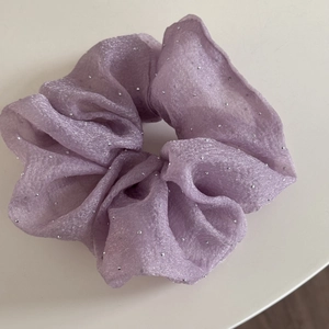 Gros plan d'un chouchou en maille lilas orné de strass argentés brillants sur fond blanc
