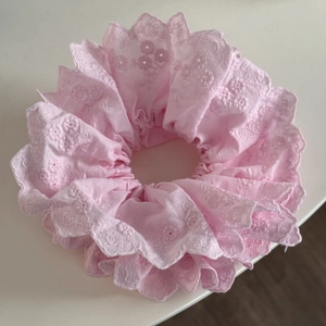 Détail du chouchou en coton rose avec broderie florale et bords festonnés en dentelle