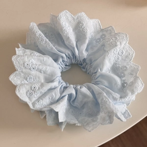 Détail d'un chouchou bleu clair avec broderie florale blanche et bordure en dentelle