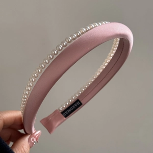 Detail of pink satin headband with white pearls and handmade woven label on grey background