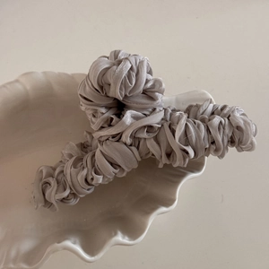 Close-up of a large grey satin pleated claw clip displayed in a white shell porcelain tray