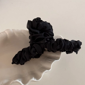 Detail view of a large black fabric rose hair claw with layered pleated silk petals