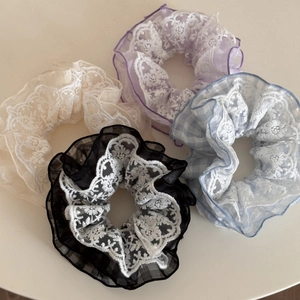 Close-up of four floral lace scrunchies in cream, lavender, and plaid patterns