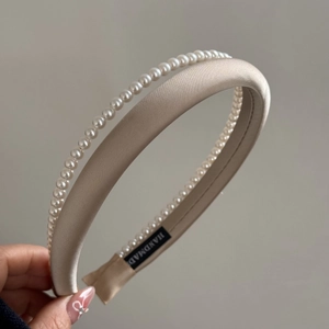 Close-up of handmade double-layer pearl headband with beige satin fabric and label
