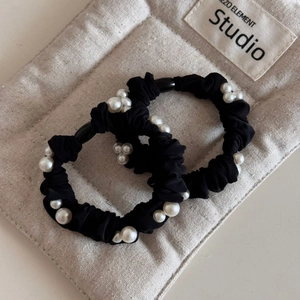 Elegant set of two black silk scrunchies with white pearls on a beige canvas background
