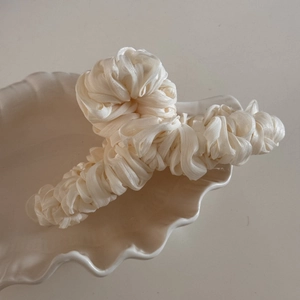 Detail of cream silk pleated hair claw clip displayed in a white ceramic shell tray