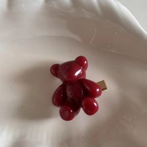 Detail view of a dark red cartoon bear hair clip in a white ceramic tray decoration