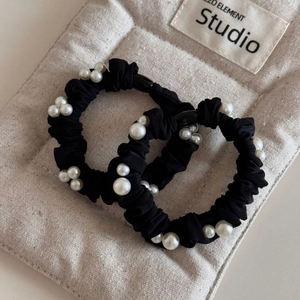 Detailed texture of black silk scrunchies with elegant white pearls on beige fabric