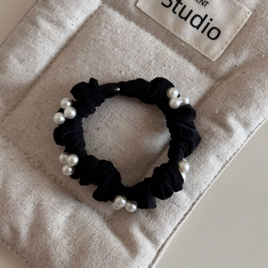 Detail of a black elastic scrunchie featuring cluster faux pearls on beige canvas