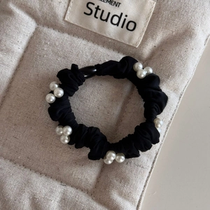 Macro detail of black scrunchie with white pearl clusters on a beige textured background
