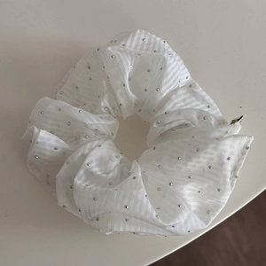 Détail d'un chouchou en tissu rayé blanc avec rivets argentés et étiquette de marque