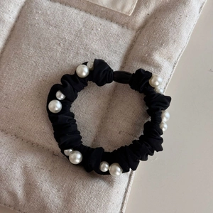 Detail view of black silk scrunchie with white imitation pearls on a beige textured background