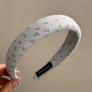 Detailed close-up of light blue floral sponge headband with a handmade woven label