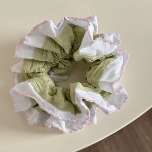 Détail d'un chouchou plissé vert clair et blanc avec une broderie rose décorative