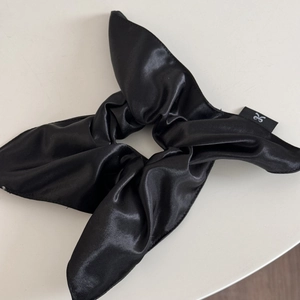 Detail of black glossy satin scrunchie with long bow and white text brand logo tag