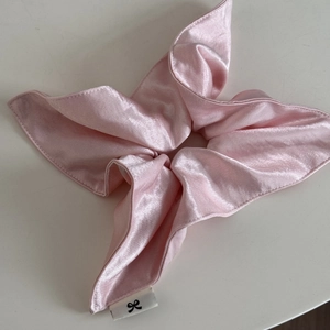 Detailed view of cream pink glossy satin scrunchie with structured petal design and logo label