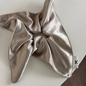 Detail of champagne gold satin scrunchie with silky finish and branded ribbon label
