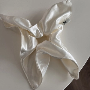 Detailed view of cream satin scrunchie with pearl luster and branded woven label