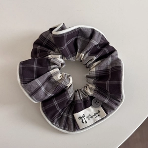Detailed close-up of grey plaid scrunchie with handmade label and button accessory
