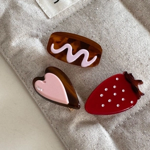 Three-piece hair clip set with strawberry and heart shapes on a beige quilted bag