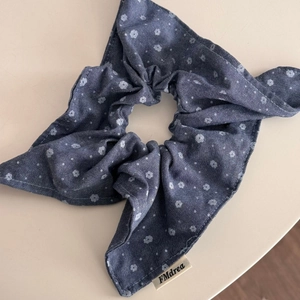 Detailed close-up of blue floral denim hair scrunchie with FMdrea brand tag and fabric texture