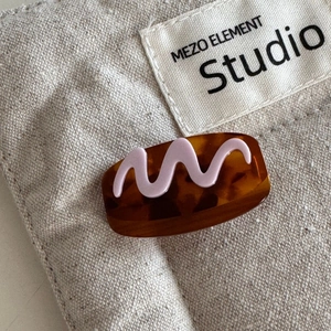 Close-up of a tortoiseshell hair clip with pink wave pattern on beige fabric