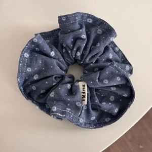 Detailed shot of denim blue floral scrunchie with polka dots and woven brand label