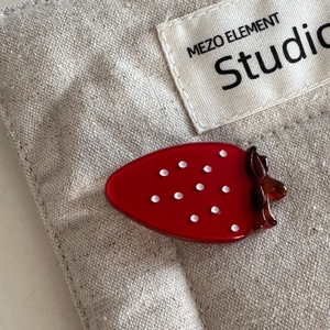 Macro shot of a red acetate strawberry hair clip with white dots on a canvas background
