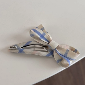 Détail d'une pince à cheveux à carreaux bleu et rose avec étiquette métallique France