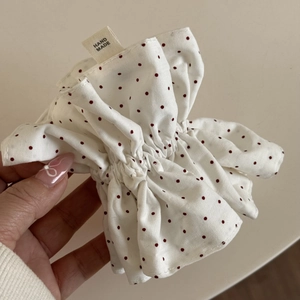 Dettaglio dell'elastico per capelli bianco a pois rossi con etichetta Hand Made