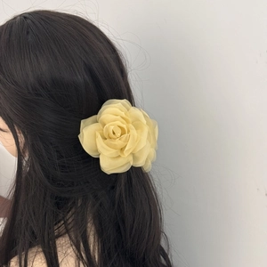 Detailed view of a light yellow chiffon rose hair claw clip on a model's dark hair