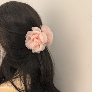 Detailed close-up of a delicate pink organza rose hair claw clip on long black curly hair
