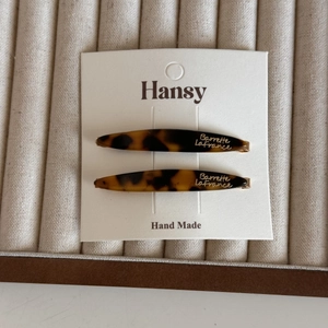 Detail of two tortoise shell acetate hair clips with gold logo on a beige jewelry tray