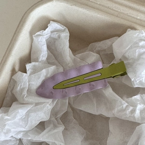 Détail de la pince à cheveux ondulée lavande avec base en métal vert olive dans sa boîte