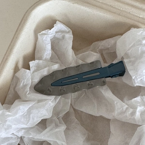 Détail d'une pince à cheveux minimaliste en métal ondulé avec une finition gris bleu foncé