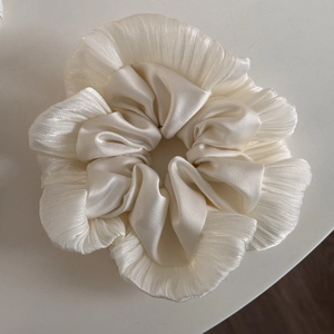 Detail of a creamy pleated satin scrunchie showing glossy texture and elegant ruffles