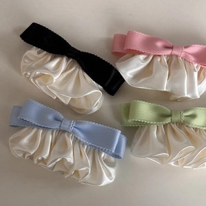 Close-up of four bow hair clips in black, pink, blue, and green with cream silk ruffles
