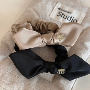 Detailed macro view of satin bow hair ties in black and beige with engraved metal charms