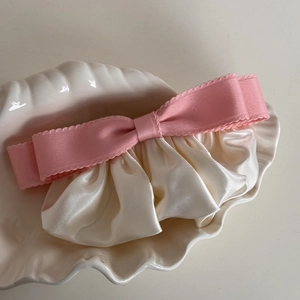 Detail of pink bow hair clip with creamy pleated satin ruffles in a shell tray