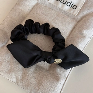 Close-up of black satin bow hair tie with a round gold charm on a textured background