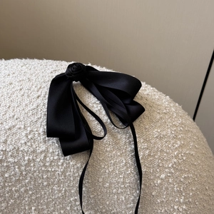 Detail of elegant black satin hair clip with a layered bow and central rose ornament